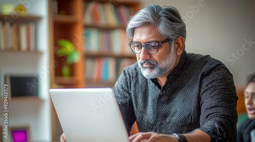 An Indian man in a black shirt works intently on his laptop in a warmly lit space photo