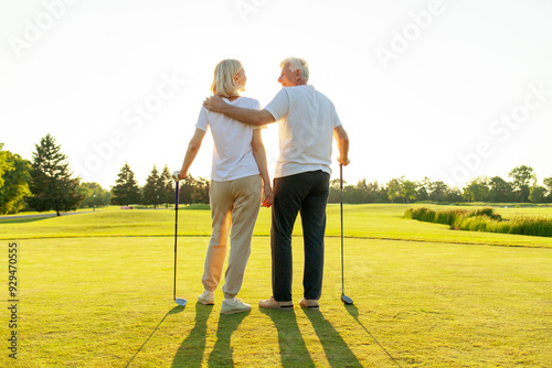 elderly senior couple in uniform playing golf on golf course at sunset, old man instructor teaching woman how to hold golf club and swing ball, grandfather helping grandmother play outdoors