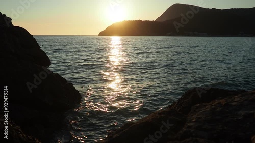 Waves gently lap at shore during stunning sunset over ocean. Golden sunlight reflects off waves as they roll onto shore, creating tranquil atmosphere at sunset by sea. Montenegro summer Canj photo