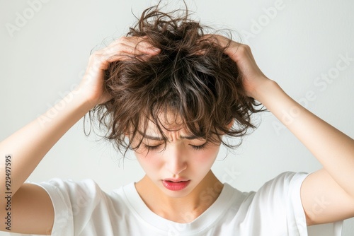 Frustrated with Frizz: A young woman with short, curly hair runs her hands through it in frustration, showcasing the common struggle of unruly hair.  The image captures the relatable feeling of battli photo