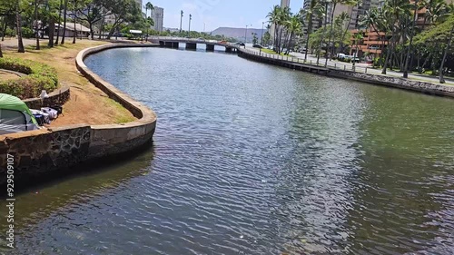 tilt footage of the Kalakaua Avenue Bridge over the Ala Wai Canal with skyscrapers hotels,, lush green palm trees, rippling water, blue sky and clouds in Honolulu Hawaii USA photo