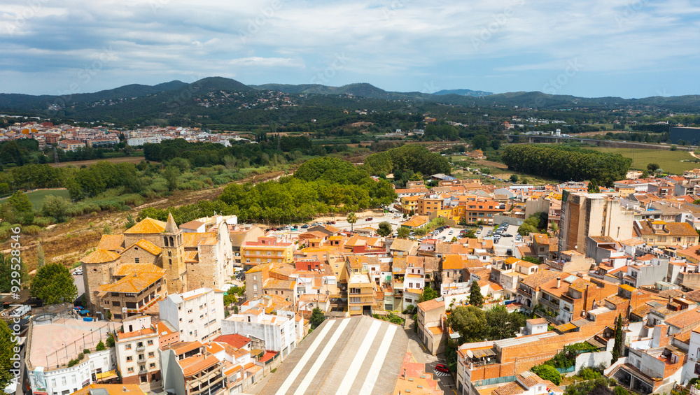 Obraz premium Scenic summer view of tiled roofs of residential houses of Spanish township of Tordera on background of greenery of Montnegre natural park on horizon on sunny day, province of Barcelona, Catalonia