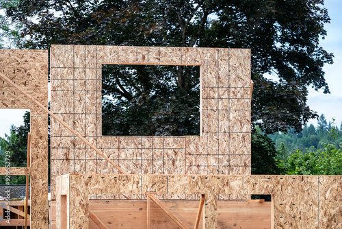 Summer construction season, closeup of second floor house support beam and exterior wall OSB, oriented strand board, sheeting with window hole cut out
 photo