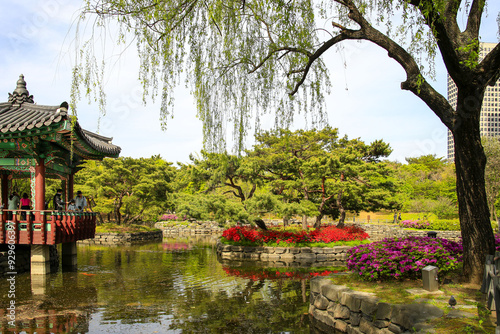 Yeouido, Yeongdeungpo-gu, Seoul, South Korea - April 23, 2022: Spring view of tourists standing in a pavilion on the pond with weeping willow and royal pink azalea flowers at Yeouido Park