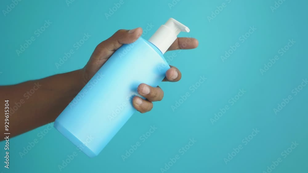 A hand is holding a blue pump bottle that stands out against a vibrant turquoise background A hand is holding a blue pump bottle that stands out against a vibrant turquoise background