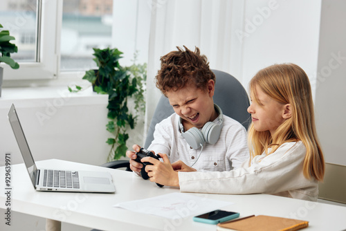 Happy children learning together with laptops and headphones in a cozy living room A boy and a girl sit at a table, studying online and typing on their computers The room is filled with excitement as