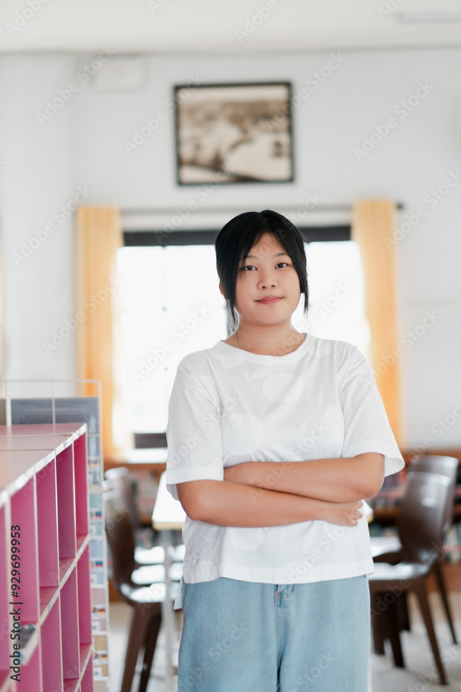 Obraz premium A young woman confidently stands with arms crossed in a bright, modern office space, showcasing a professional and determined demeanor.