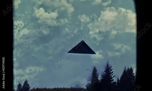 A distant view of a pyramid-shaped structure partially obscured by trees under a cloudy sky, evoking a sense of mystery and nature's beauty.