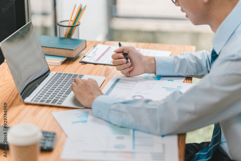 A man is sitting at a desk with a laptop and a stack of papers. He is focused on his work, possibly working on a project or report. Concept of concentration and productivity A man is sitting at a desk with a laptop and a stack of papers. He is focused on his work, possibly working on a project or report. Concept of concentration and productivity