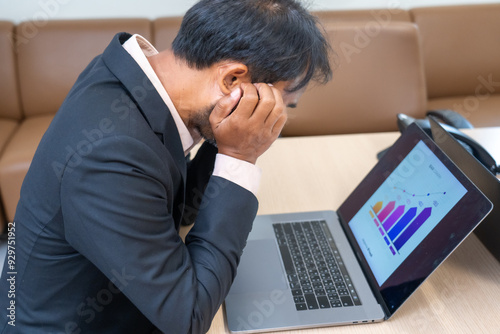 A stressed business professional looks at a laptop displaying declining charts, conveying frustration or concern.