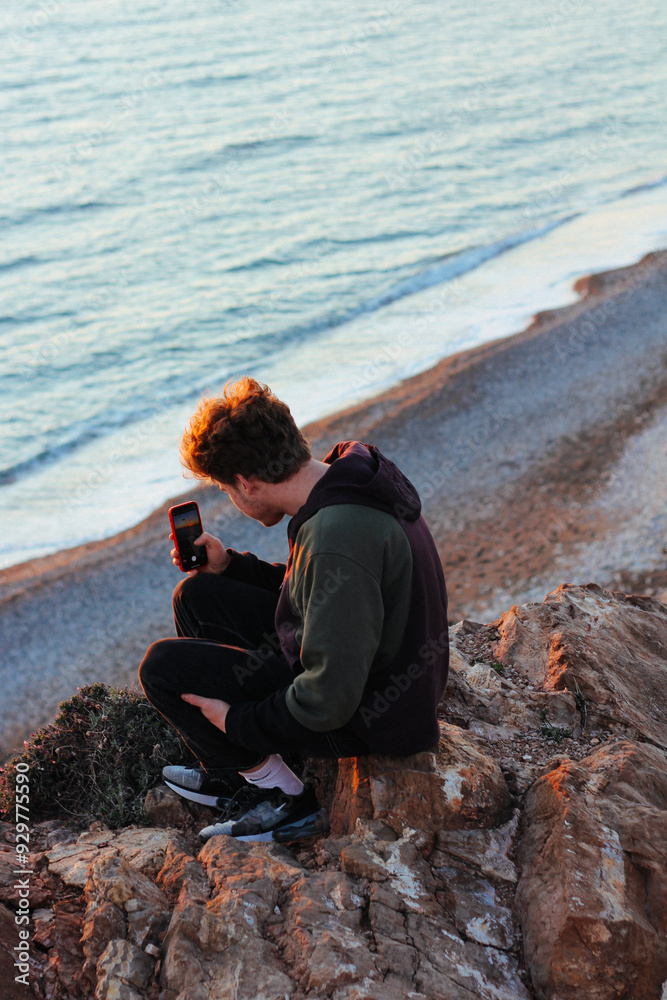 A man sits near a rocky coast and takes a picture A man sits near a rocky coast and takes a picture