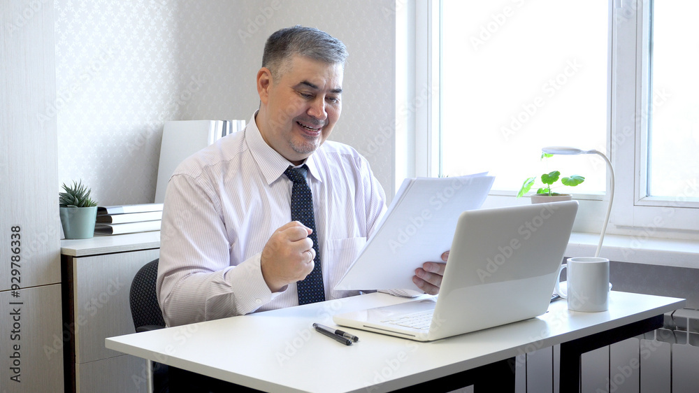 Man Reviewing Documents and Smiling at Office Desk Man Reviewing Documents and Smiling at Office Desk