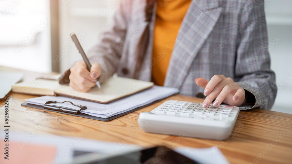 A close-up image of a businesswoman using a calculator and taking notes in her notebook. A close-up image of a businesswoman using a calculator and taking notes in her notebook.