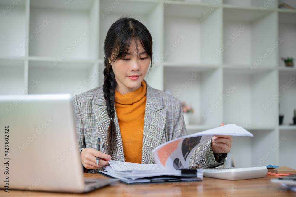 A positive Asian businesswoman is reviewing the financial report while working at her desk. A positive Asian businesswoman is reviewing the financial report while working at her desk.