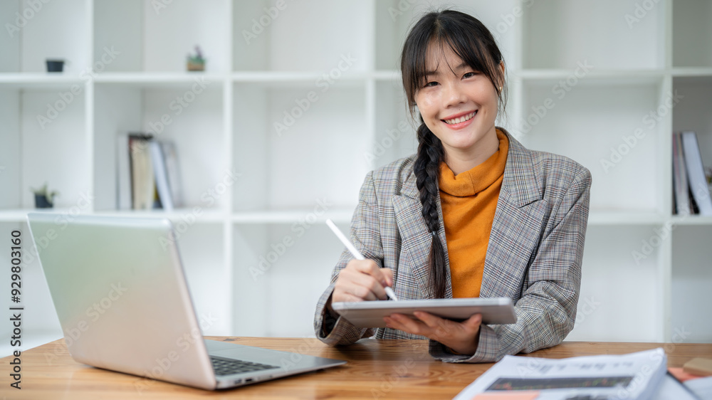 A businesswoman is smiling at the camera, sitting at her desk with a digital tablet in her hand. A businesswoman is smiling at the camera, sitting at her desk with a digital tablet in her hand.