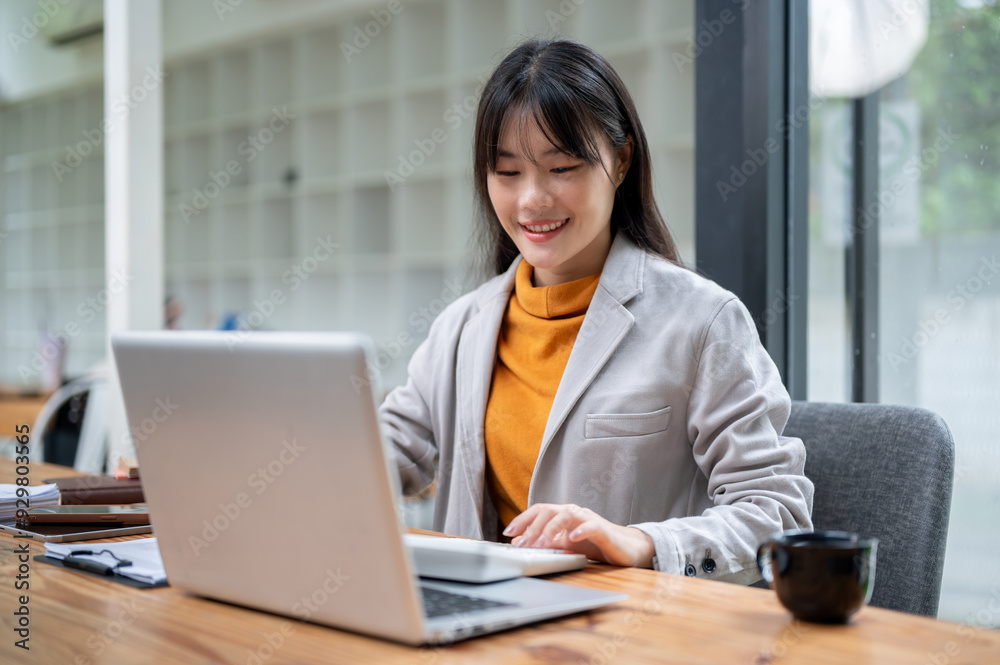 A charming Asian businesswoman or female accountant is using a calculator and working at her desk. A charming Asian businesswoman or female accountant is using a calculator and working at her desk.