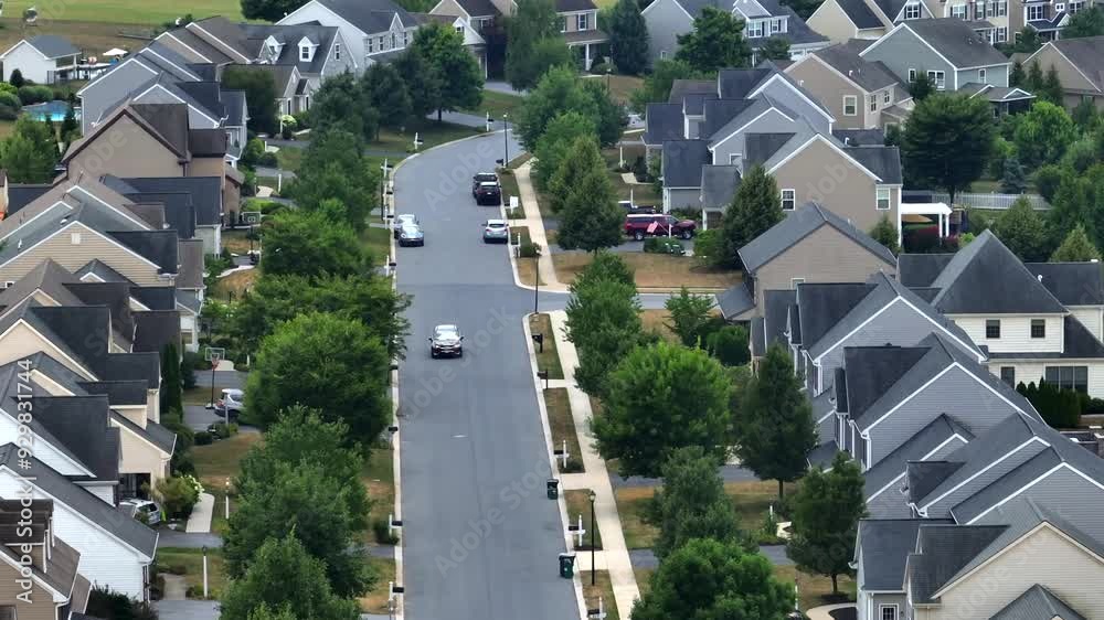Suburban neighborhood with single family homes. Rows of houses with driveways. Car on street turning into straight road. Rural residential community in USA during summer. Aerial zoom shot. Suburban neighborhood with single family homes. Rows of houses with driveways. Car on street turning into straight road. Rural residential community in USA during summer. Aerial zoom shot.
