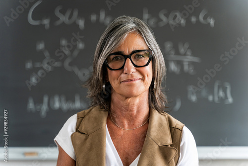 Mature female professor standing at college classroom looking at camera. Elegant School woman teacher  photo