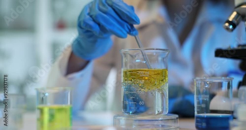 Scientist mixes yellow liquid in laboratory beaker