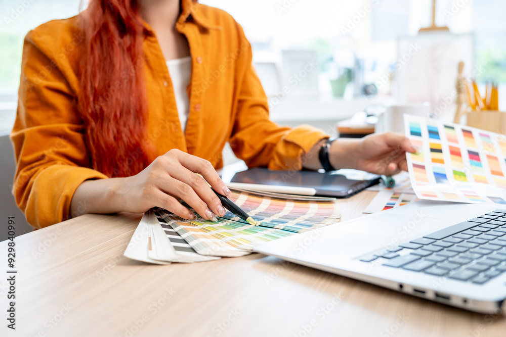 A female graphic designer working at her desk in the studio, selecting colors from a set of swatches A female graphic designer working at her desk in the studio, selecting colors from a set of swatches