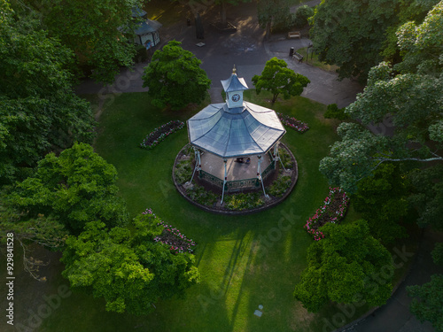 Beautiful bandstand with old clock in Swindon Town Gardens at sunset. Aerial view of historic landmark surrounded with flower beds and green trees creating shade in the summer. Peaceful environment.