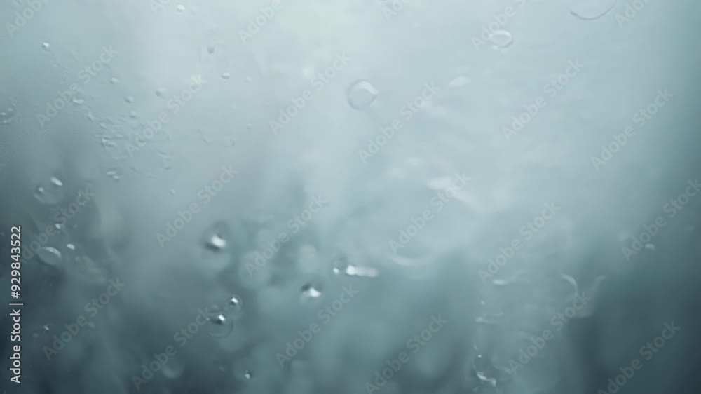 Water condensation forms on a glass surface, creating a visually appealing texture against a light background. The scene captures droplets and vapor, highlighting humidity and coolness