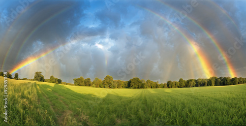 A panoramic view of a field with a rainbow visible in the clear sky after the rain