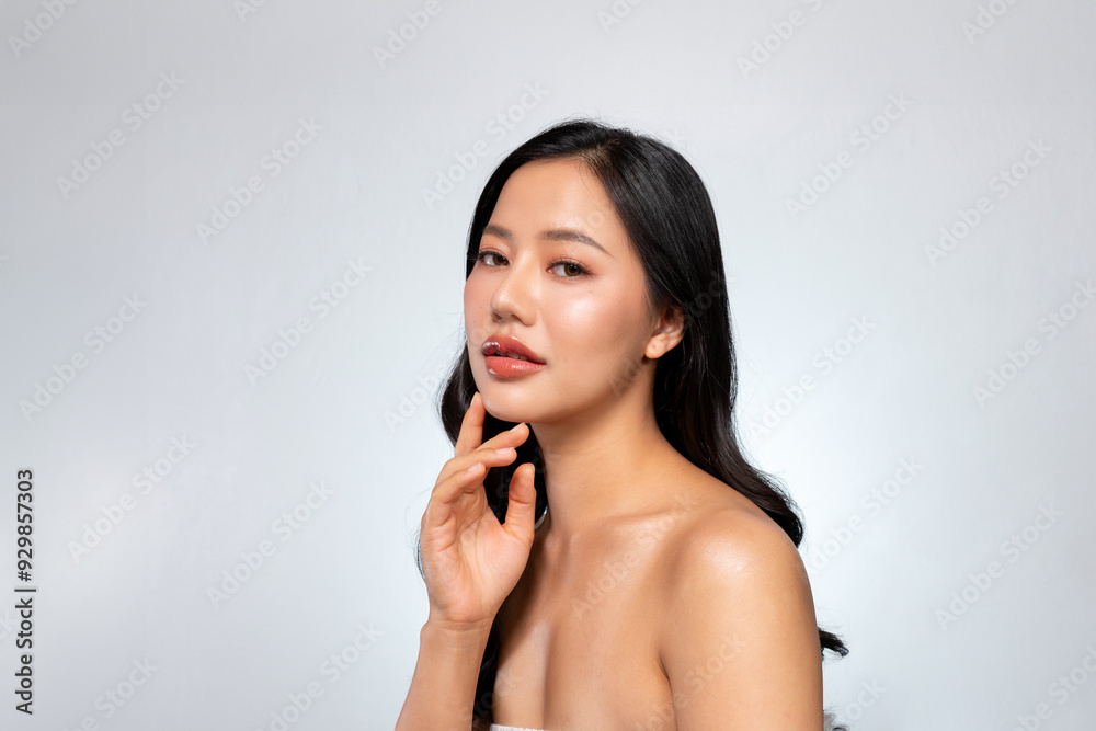 Elegant Asian woman poses against a grey background, looking at the camera while touching her chin. Elegant Asian woman poses against a grey background, looking at the camera while touching her chin.