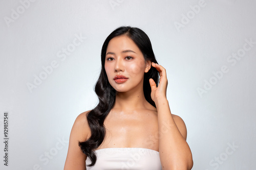 Beautiful Asian woman with healthy black curly hair and tanned skin poses against a grey background.