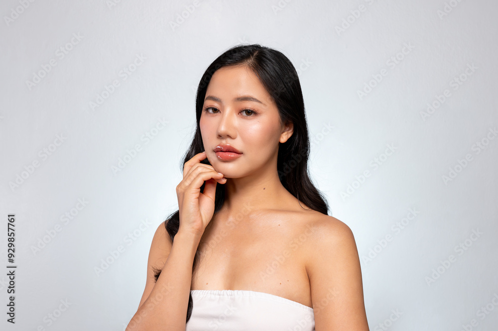 Gorgeous Asian woman with a beautiful face poses against a grey background, gently touching her chin Gorgeous Asian woman with a beautiful face poses against a grey background, gently touching her chin