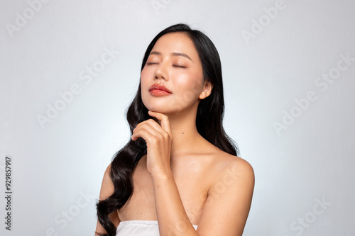 A young Asian beauty poses against a grey background, gently touching her face with her eyes closed.