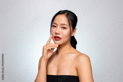 A beautiful Asian woman with perfect makeup and tanned skin poses against a grey studio background.