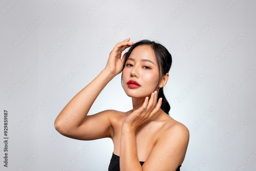 A young Asian woman with a perfect, beautiful face poses against a grey background, touches her face A young Asian woman with a perfect, beautiful face poses against a grey background, touches her face