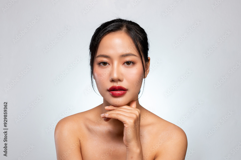 A beautiful Asian woman with red lips, and tanned skin poses against an isolated grey background. A beautiful Asian woman with red lips, and tanned skin poses against an isolated grey background.