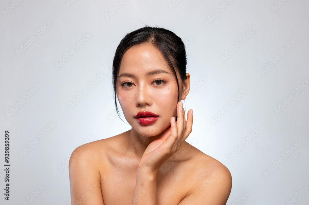 A beautiful Asian woman with red lips, and tanned skin poses against an isolated grey background. A beautiful Asian woman with red lips, and tanned skin poses against an isolated grey background.