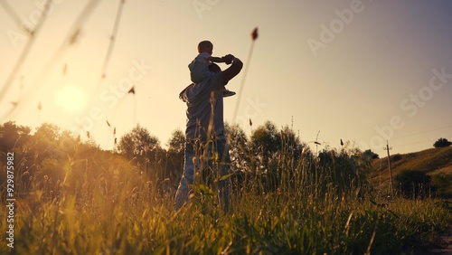 father carries a little son on his shoulders and walks on the grass in the park. happy family childhood dream concept. a small child sits on the shoulders of his lifestyle dad man walking in field