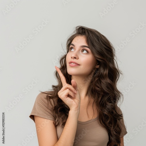 A beautiful young woman pointing diagonally upward to her right, isolated on a light gray background. 