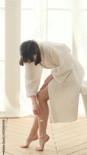 Joyful Caucasian middle aged woman engaged in leg depilation procedure at home bathroom. Concept of a beauty treatment. Vertical video.