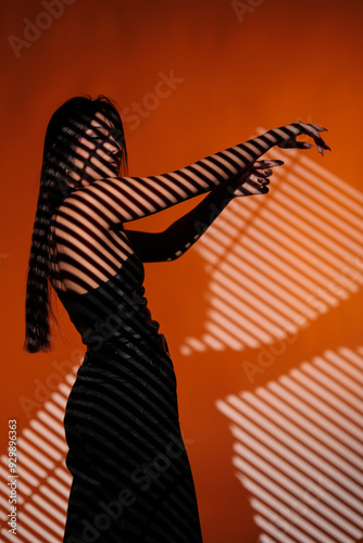 Brunette girl posing in a beam of light in the studio, on a red background, light and darkness.