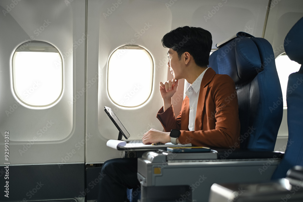 Thoughtful young businessman sitting in an airplane seat with digital tablet and looking through window Thoughtful young businessman sitting in an airplane seat with digital tablet and looking through window
