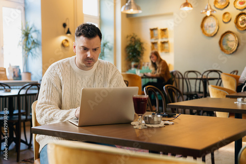 Man in sweater working on laptop in a cafe