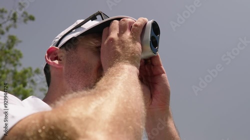 Male golfer uses rangefinder on golf course during sunny summer day, close up slow motion