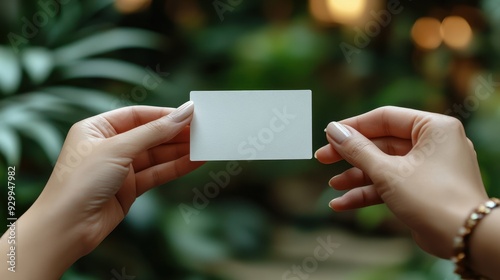 Close-Up of Two Hands Holding a Business Card - One Hand Passing Blank White Card to Another Against Natural Background