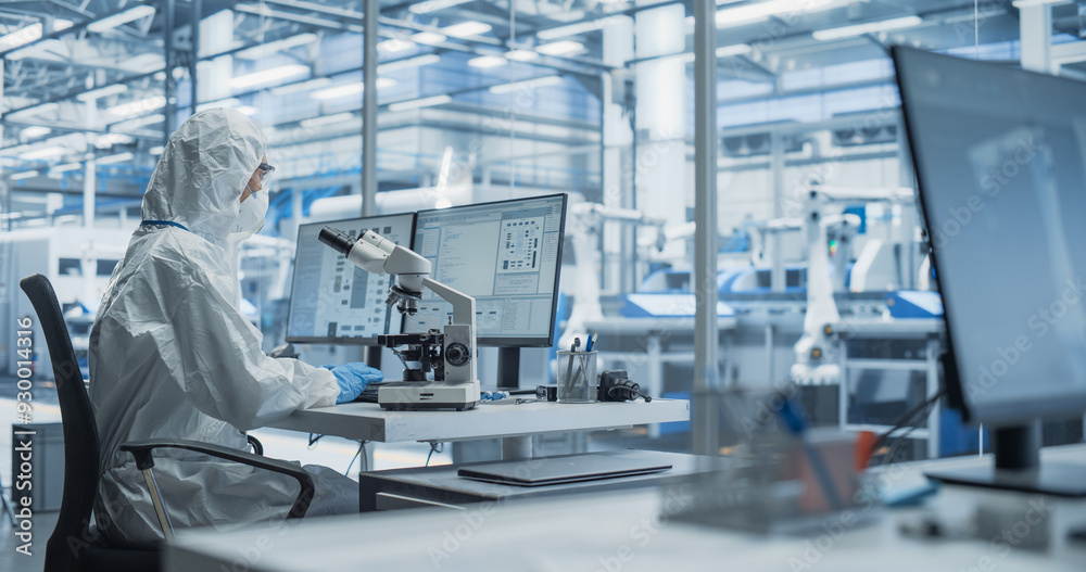 © Gorodenkoff - Modern Factory: Industrial Engineer Working on Desktop Computer in Clean Sterile Coveralls. Scientist Using a Microscope, Developing Advanced Solutions for High Tech Medical Vaccine and Gene Research