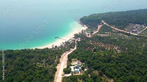 Drone flies back over island filled with green trees, roadway with resorts and wide ocean view at Kon rong island in sihanouk ville province. photo