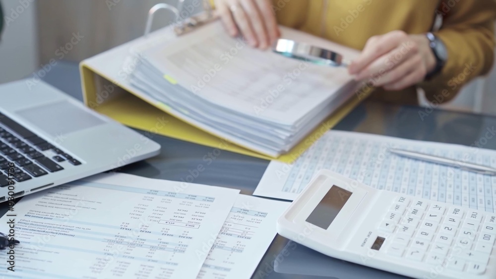 Close-up of a calculator and financial papers are in focus. Female professional working with spreadsheets and a laptop on the background. Business audit and taxes