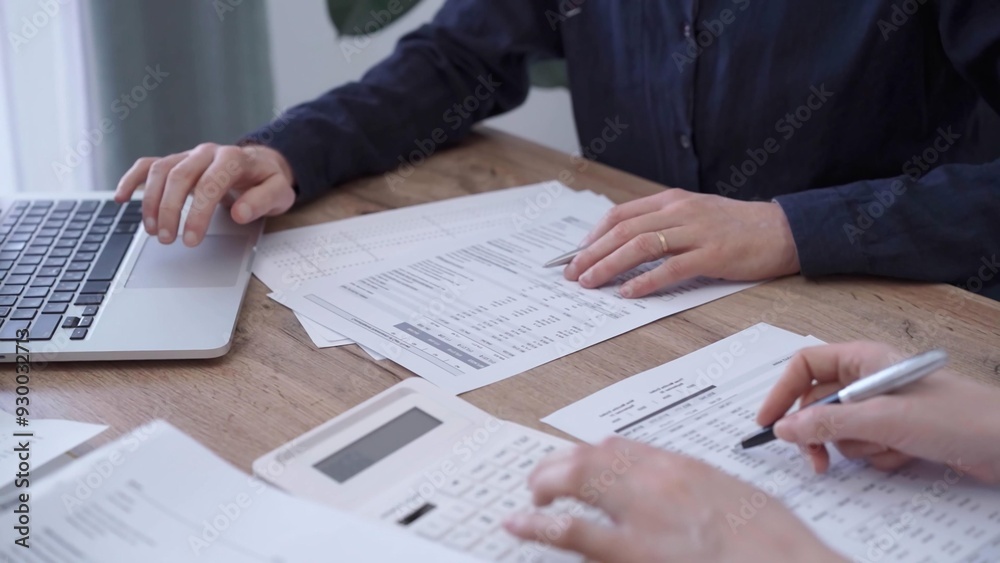 Close up of professional hands using a calculator to conduct financial analysis at the background of a colleague with a magnificent glass. Bookkeeping, finance audit and taxes Close up of professional hands using a calculator to conduct financial analysis at the background of a colleague with a magnificent glass. Bookkeeping, finance audit and taxes