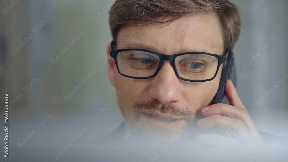 Businessman with glasses speaking on the phone, partially obscured by blurred laptop. Front view and close up portrait Businessman with glasses speaking on the phone, partially obscured by blurred laptop. Front view and close up portrait