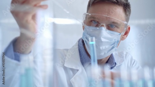 Man with safety glasses and blue mask is working with lab tubes using a pipette in a modern laboratory, close-up of researcher. Science and medicine