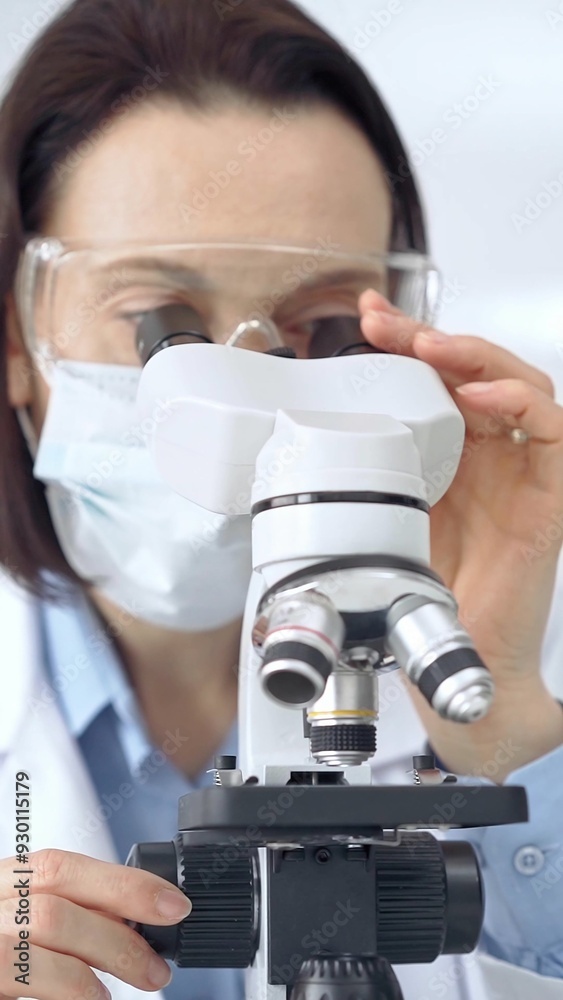 Female scientist using microscope in laboratory. Focus on a woman in lab goggles analyzing samples with a microscope in a scientific setting Female scientist using microscope in laboratory. Focus on a woman in lab goggles analyzing samples with a microscope in a scientific setting
